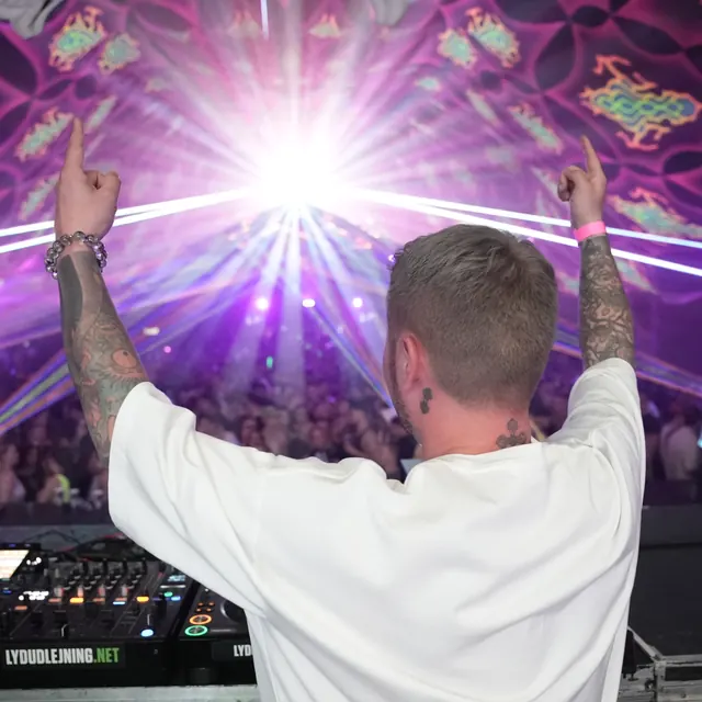 DJ set bagfra med begge arme løftet mod publikum og laserlyset.