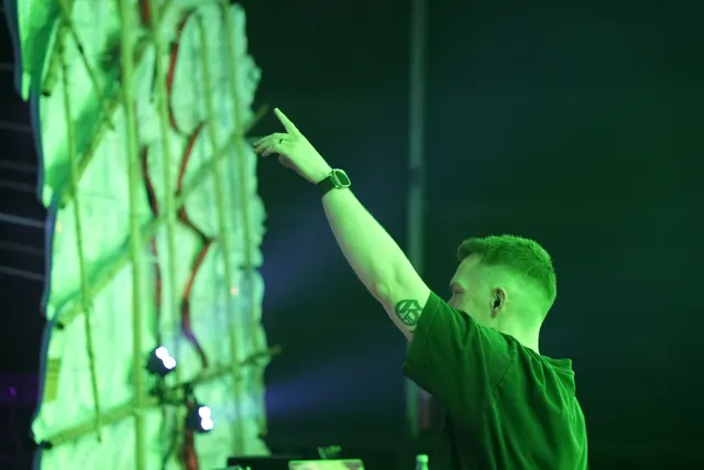 DJ ved pulten med en arm løftet i grønt scenelys.