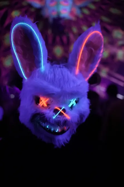 Festivalgæst med en lysende kaninmaske mod en mørk baggrund.