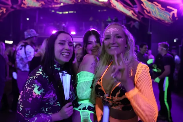 Tre smilende festivalgæster i orange og grønne neonfarver.