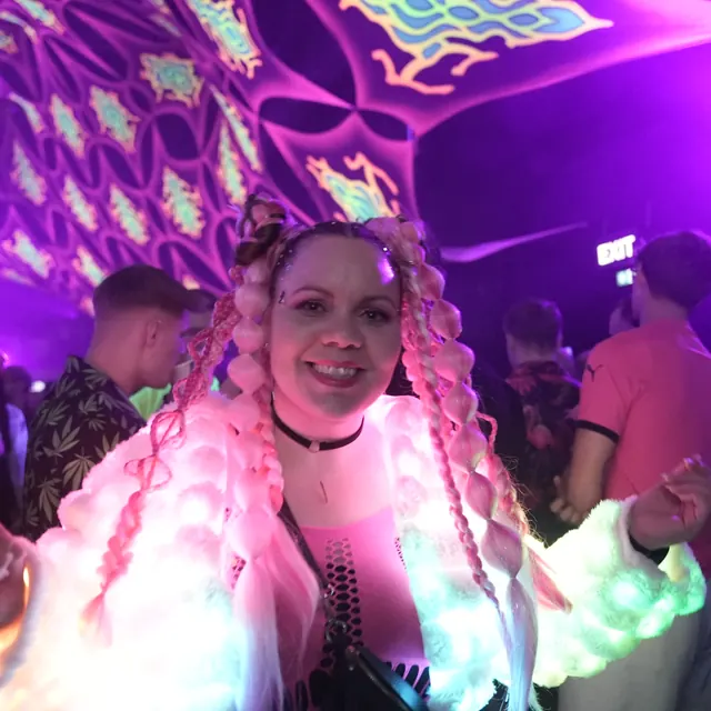 Festivalgæst med lyserøde fletninger og en jakke med farvede lys.