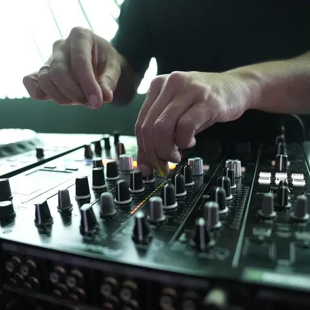 Hænder justerer knapperne på en DJ-mixer.