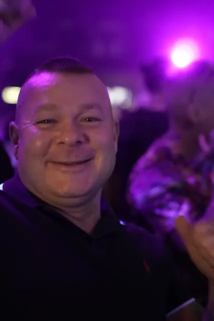 Smilende festivalgæst i sort trøje med lilla lys i baggrunden.