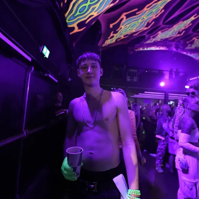 Festivalgæst med en kop og neonarmbånd foran dansegulvet.