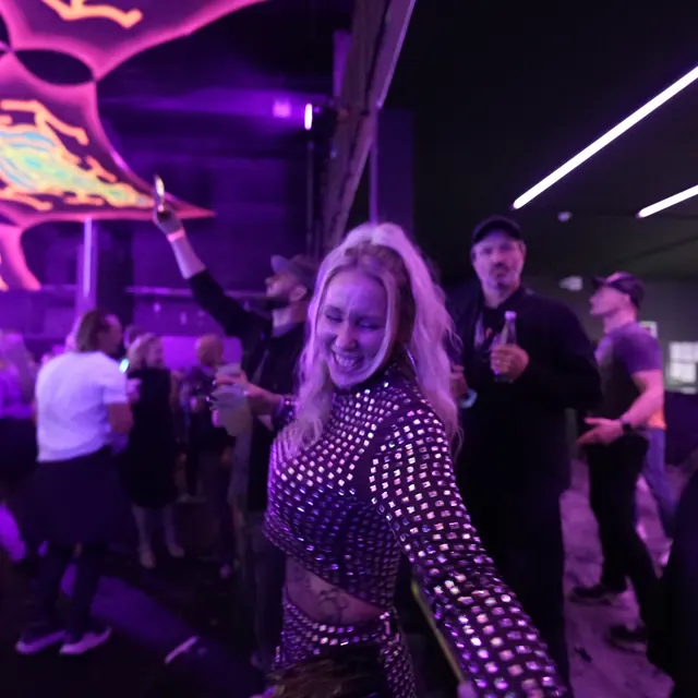 Smilende gæst danser i et sort skinnende sæt under loftsdekorationerne.