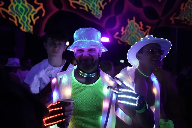 Festivalgæster med lysende hatte, handsker og neonfarver på dansegulvet.
