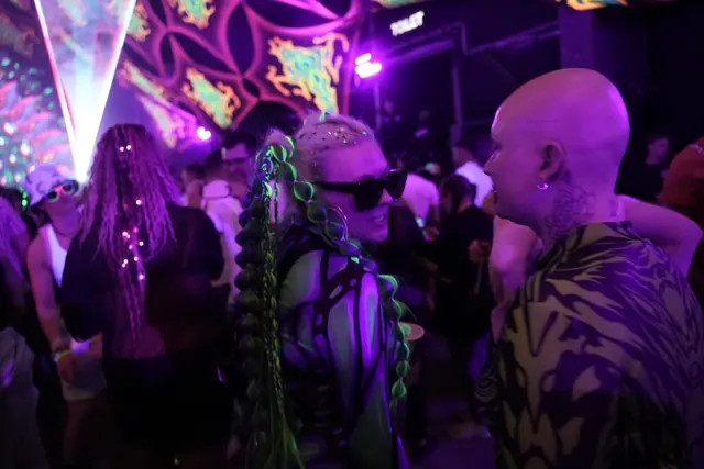 To gæster står tæt sammen på dansegulvet, den ene med grønne fletninger og solbriller.