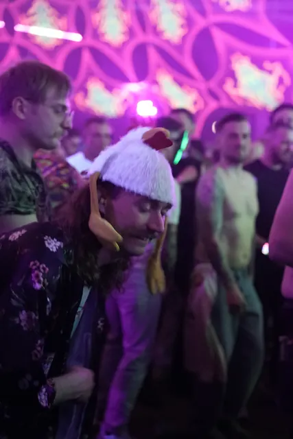 Festivalgæst med en hvid hønsehat og blomstret skjorte på dansegulvet.