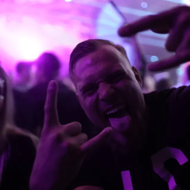 Festivalgæst laver rocktegn til kameraet i lilla lys.