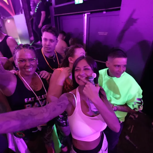 En gruppe gæster poserer sammen i pink og grønt lys ved dansegulvet.