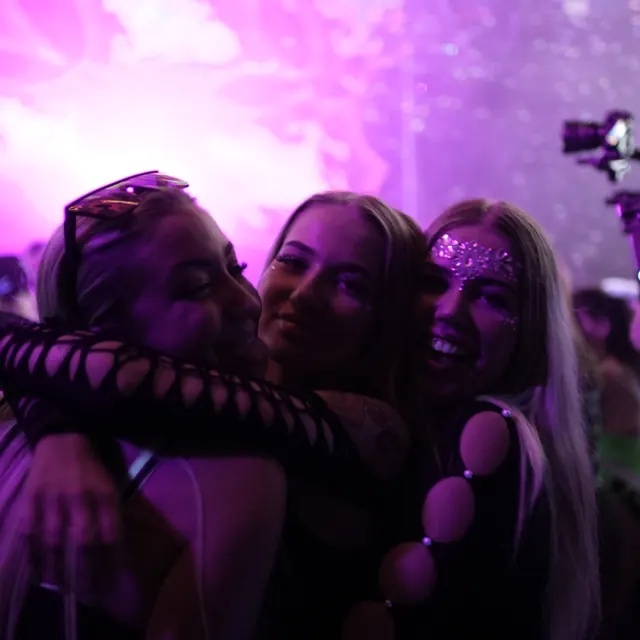 Tre festivalgæster står tæt sammen og poserer i lilla scenelys.
