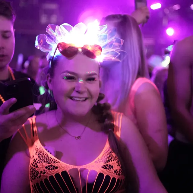 Smilende festivalgæst med orange neonoverdel og en lysende krone.