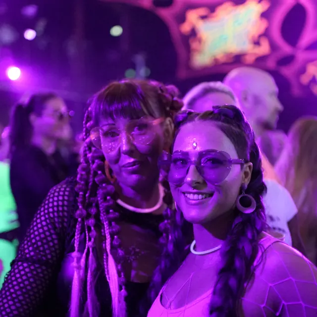 To festivalgæster med fletninger, briller og neonhalskæder smiler til kameraet.