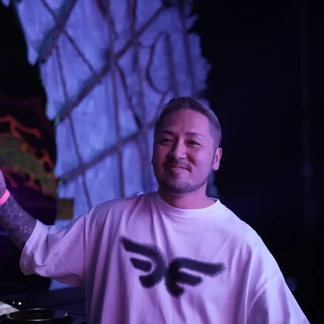 Smilende DJ i en hvid T-shirt ved pulten i lilla scenelys.