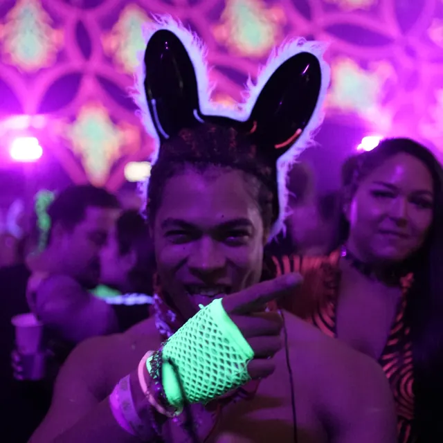 Festivalgæst med sorte kaninører og neongrøn handske poserer med en gæst i baggrunden.