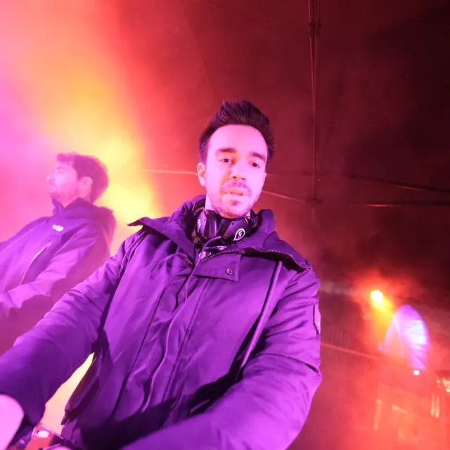 DJ med hovedtelefoner om halsen ved pulten i orange og pink lys.