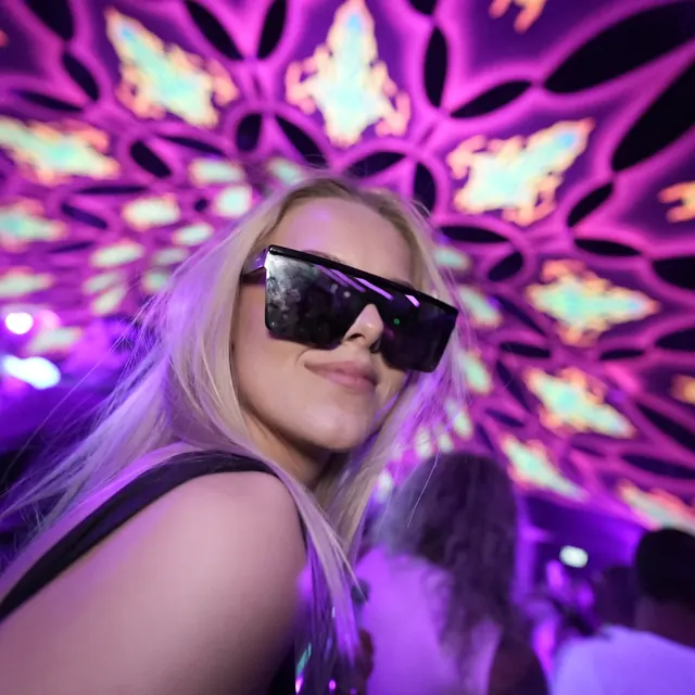 Festivalgæst med store sorte solbriller under lilla loftsdekorationer.